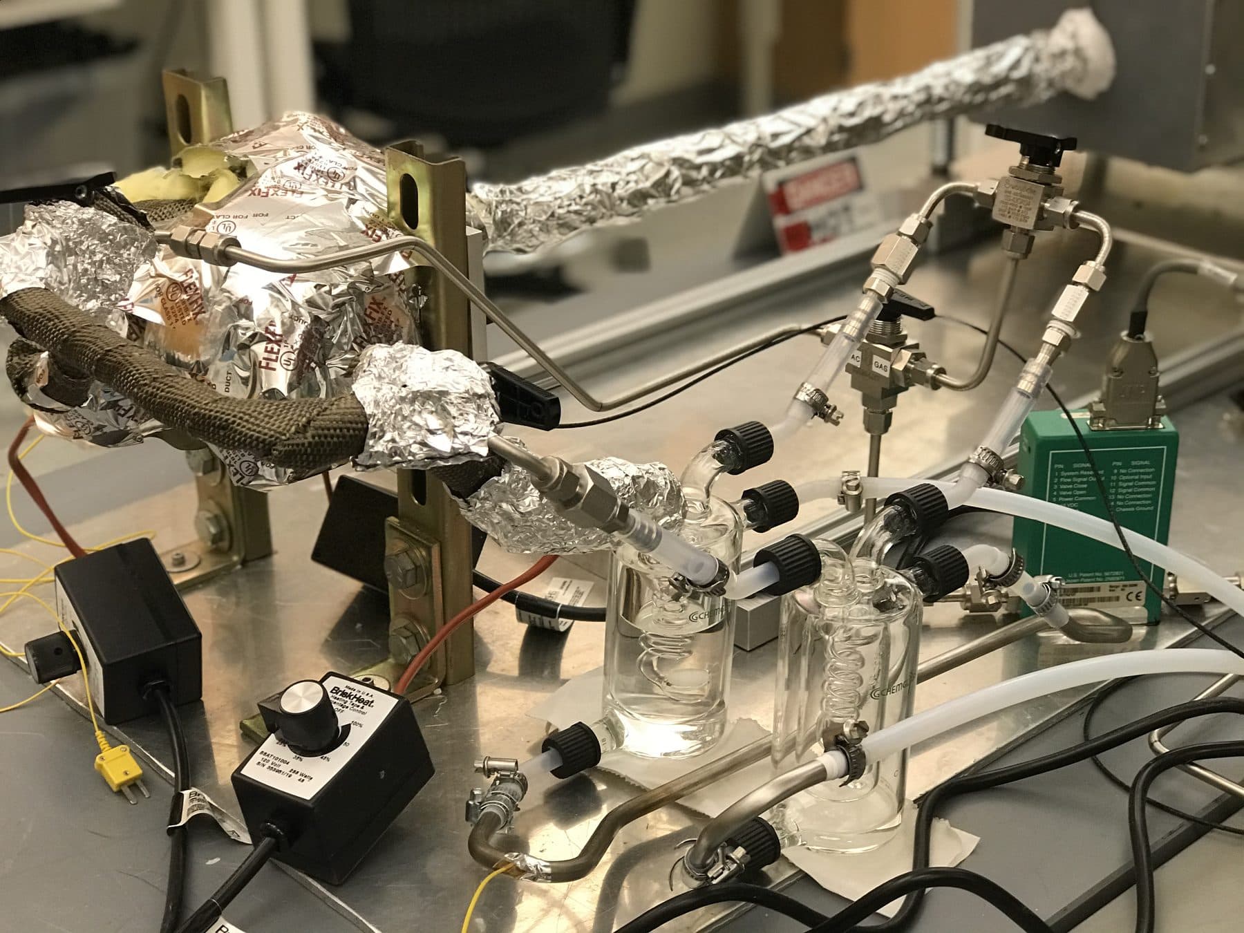 A custom-built research apparatus with heat-traced lines, glass bubblers, thermocouples and a stainless steel gas manifold on a bench