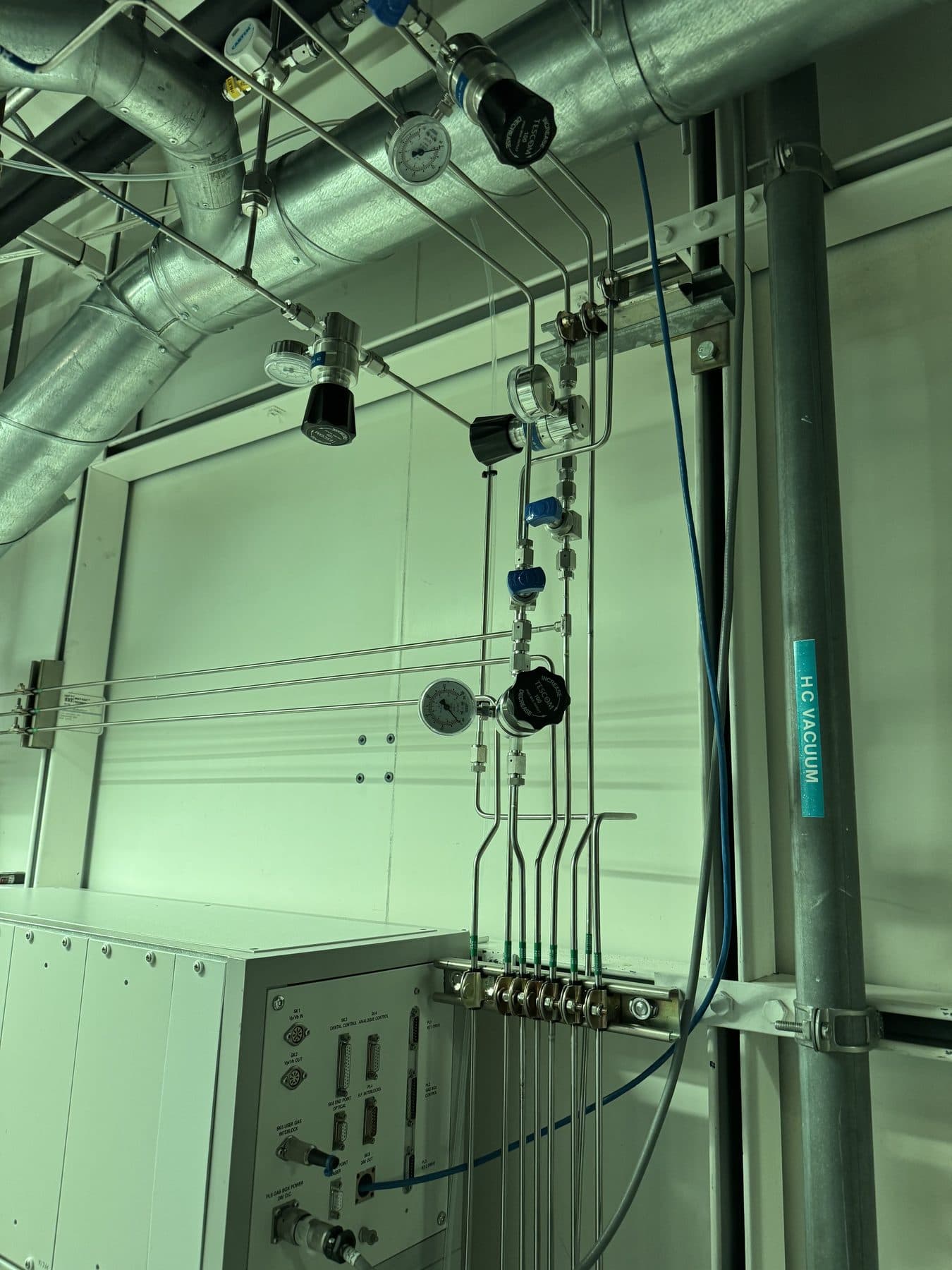 Bent stainless steel tube runs with regulators and gauges delivering gas into the service panel of a process tool